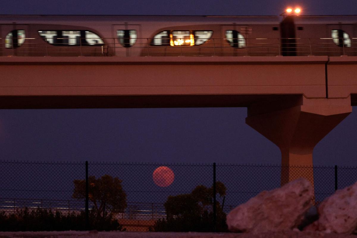 The full moon rises on the horizon as a metro train passes in Doha on October 7, 2025. (Photo by Karim JAAFAR / AFP)