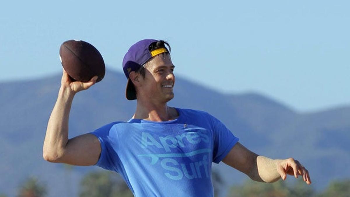 Josh Duhamel con la pelota de fútbol americano en la playa