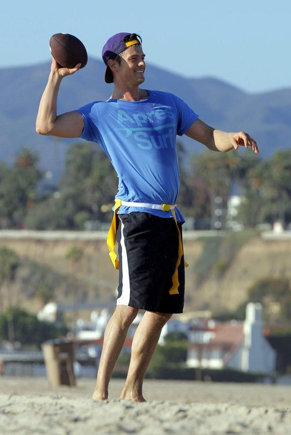 Josh Duhamel con la pelota de fútbol americano en la playa