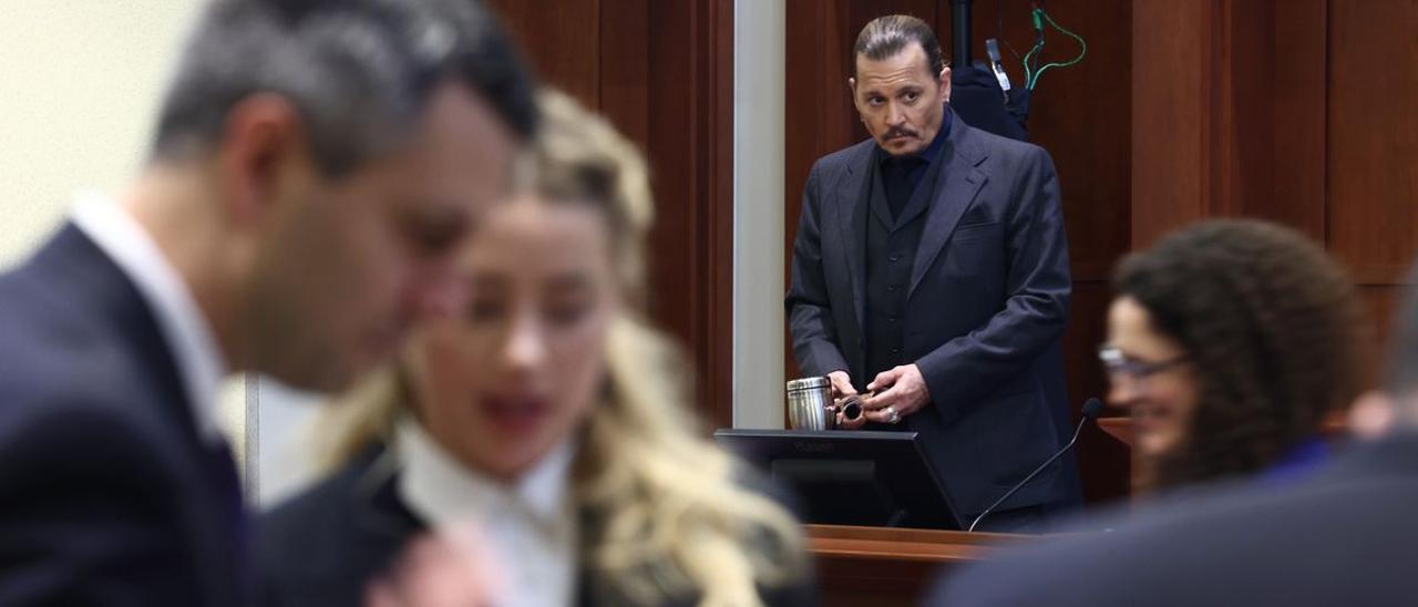 Amber Heard, desenfocada en primer plano, y Johnny Depp, durante el juicio.