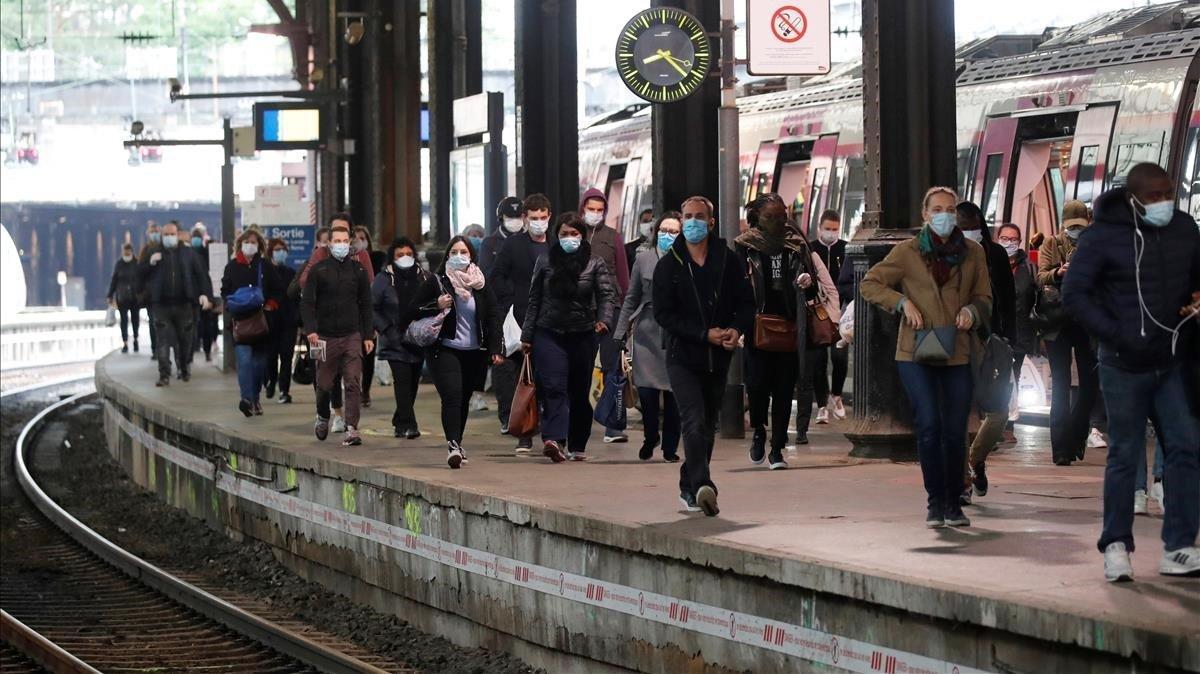 Los viajeros, que usan máscaras faciales protectoras, caminan en una plataforma en la estación de tren de Saint-Lazare en París