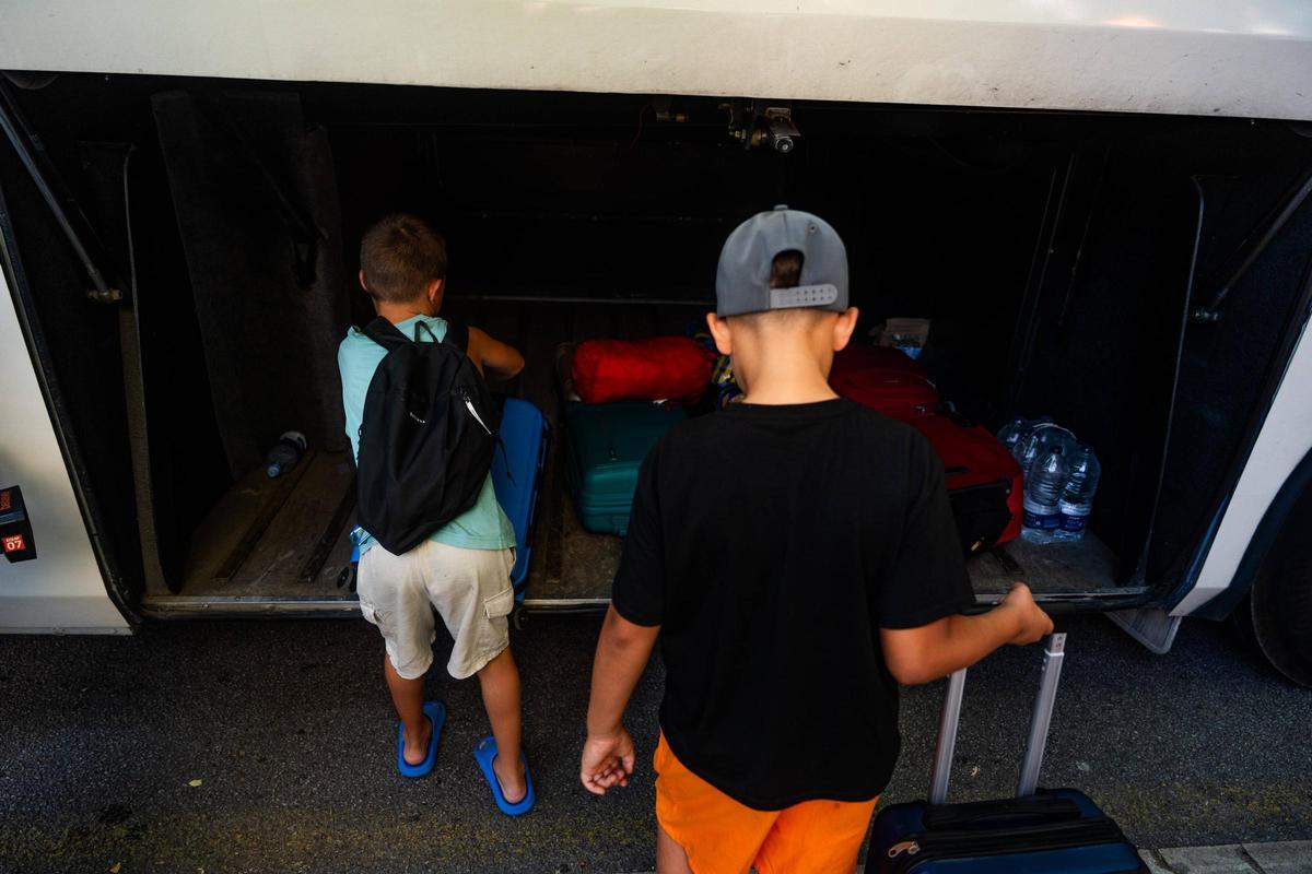 Dos niños meten sus mochilas en un autocar para irse de colonias.