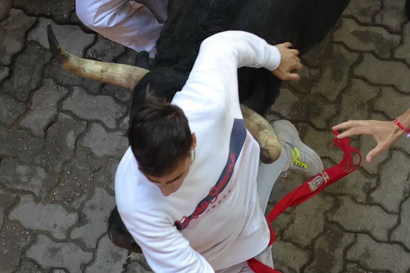 PAMPLONA, 13/07/2025.- Uno de los toros engancha el pitón bajo la camiseta de  uno de los mozos en el tramo final que desemboca en el callejón de la Plaza de Toros durante el séptimo encierro de los Sanfermines 2025 este domingo en Pamplona. EFE/ J.P. Urdiroz