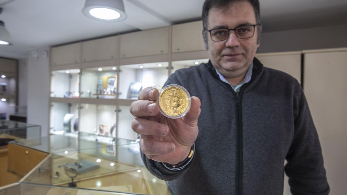 Juan Cardell muestra una moneda con el símbolo del bitcoin en su relojería de Alicante.