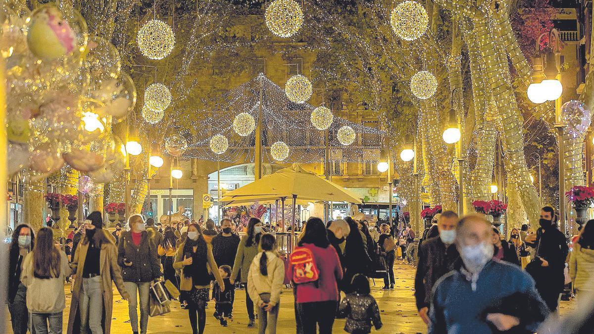 Ciudadanos paseando con mascarilla por las calles de Palma iluminadas por Navidad.