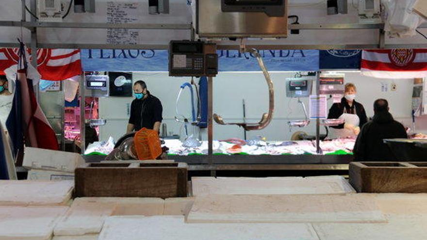 En primer pla, una peixateria del Mercat del Lleó de Girona tancada i, al fons, dues atenent clients