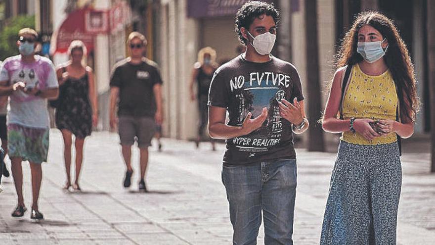 Dos jóvenes caminan por la calle Castillo de Santa Cruz con mascarilla.
