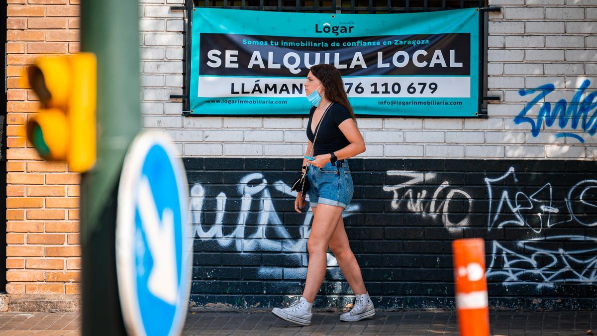 Una joven pasea por Zaragoza frente a un cartel de alquiler.
