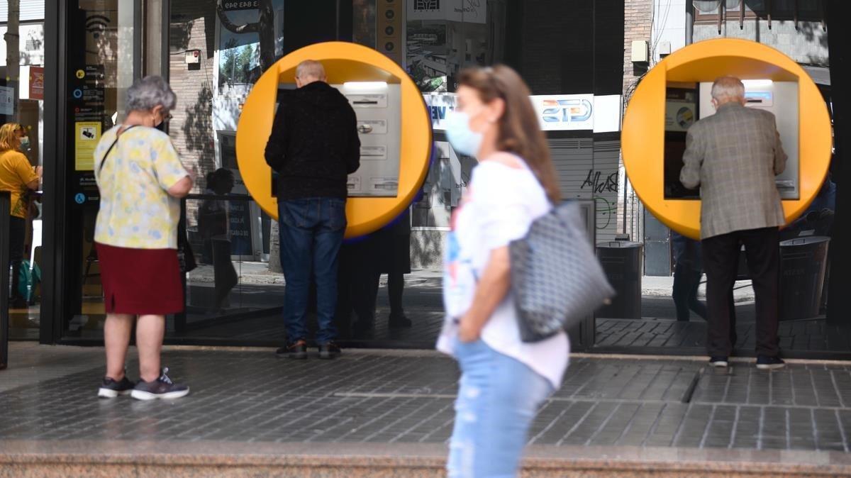 Varias personas sacan efectivo en un cajero en una oficina bancaria en Barcelona.