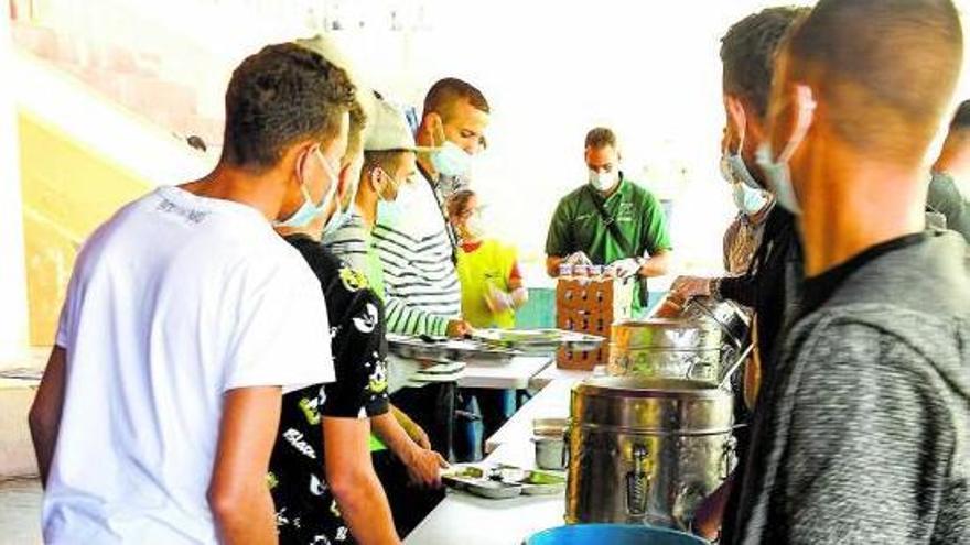 Algunos migrantes esperan su turno en el comedor del centro de acogida en el Colegio León en El Lasso.