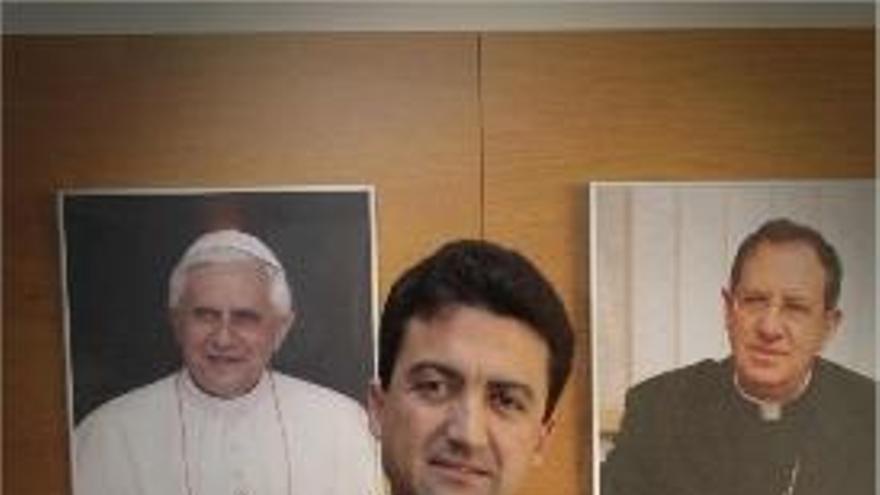 El sacerdote, entre los retratos del Papa y el obispo.