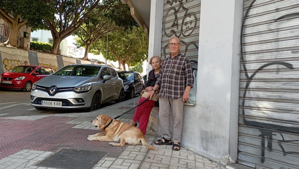 Ángel y Conchi, se tiene que sentar en los bordes de los escaparates a falta de bancos en Marqués de Ovieco. Detras, los cinco famosos ficus, la única 'mancha verde' de la zona.