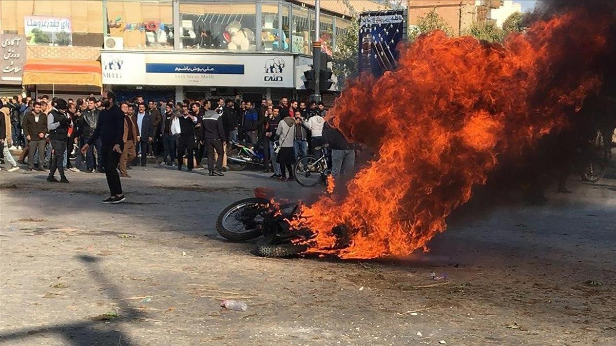 Manifestantes iranís junto a una motocicleta quemada en Isfahan (Irán).
