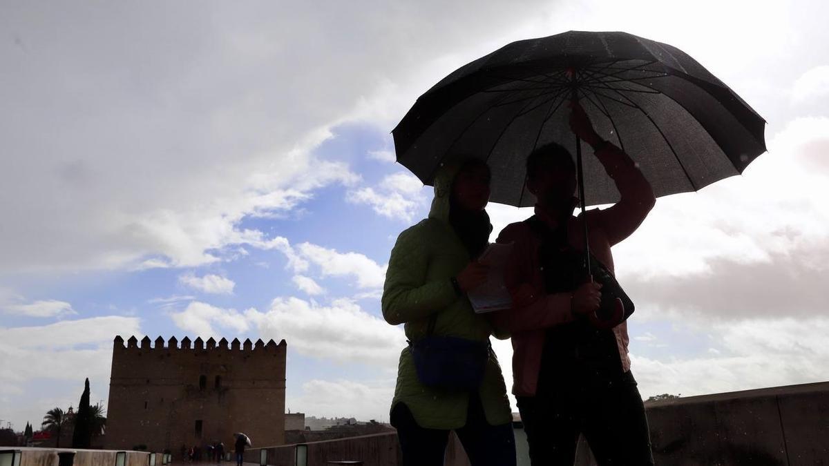 Una pareja se protege de la lluvia con un paraguas en el Puente Romano de Córdoba.