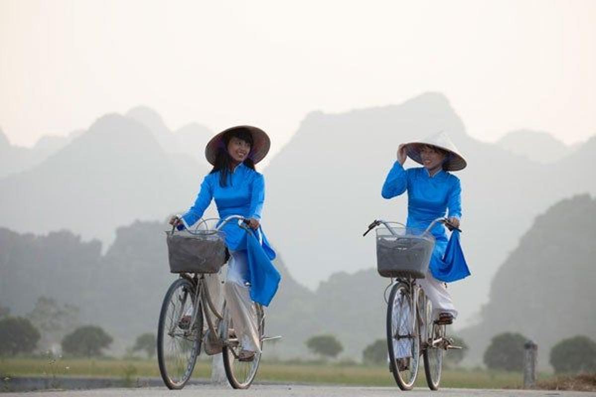 Chicas jóvenes montando en bici vestidas con ropas tradicionales cerca de Hanoi, en Vietnam.