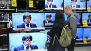 Expectación 8 Una pareja sigue la rueda de prensa de Puigdemont en una tienda del Poblenou.