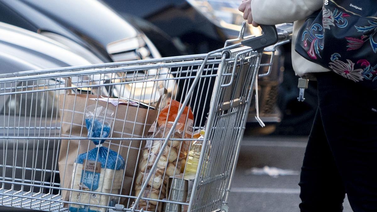 mujer sale del supermercado con el carro de la compra.