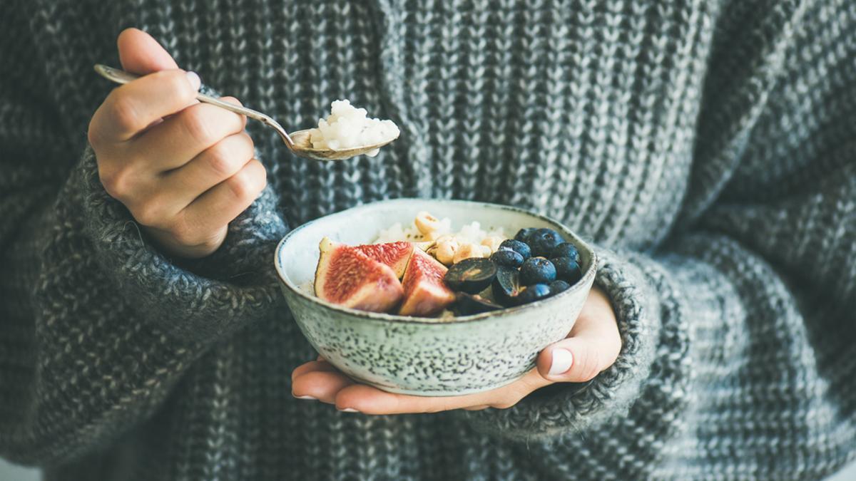 Una mujer desayuna un bowl de fruta.