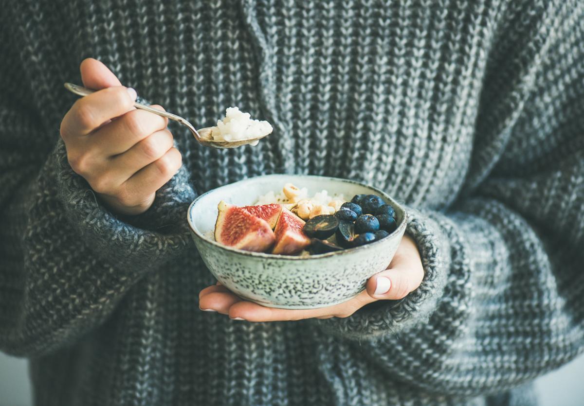 Una mujer desayuna un bowl de fruta.
