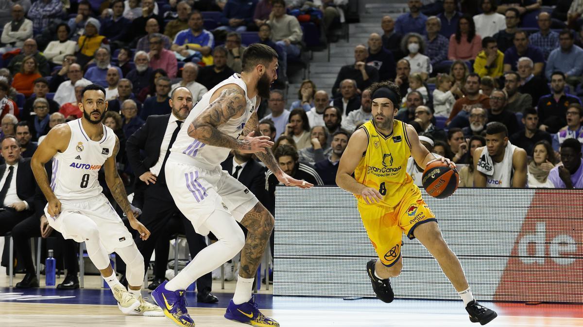 Vítor Benite bota el balón ante la oposición de Vincent Poirier, del Real Madrid, y su compañero merengue Adam Hanga –8–, en un partido de liga regular de la Liga Endesa.