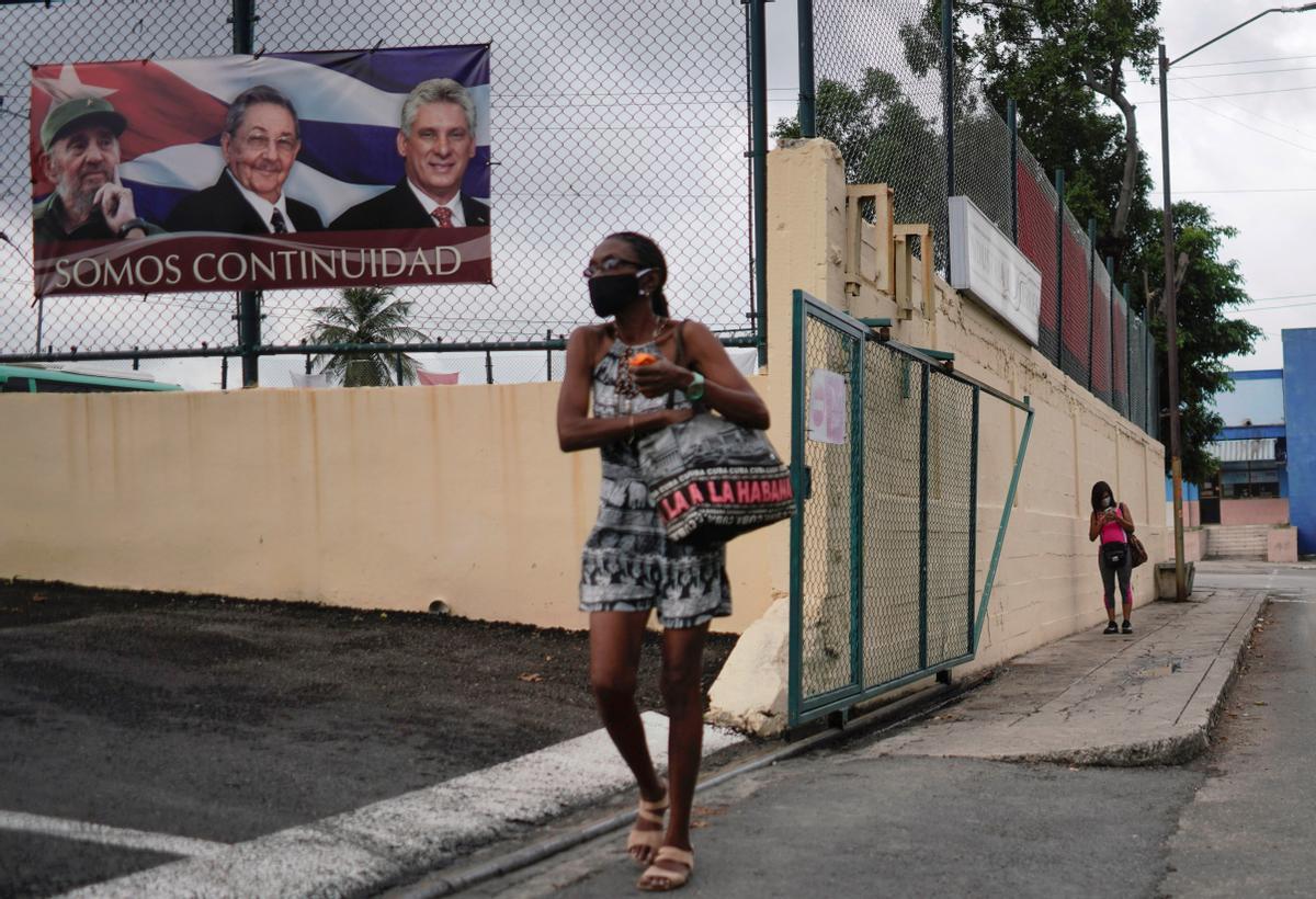 Una mujer pasa junto a un cartel con las fotografías de Fidel Casto, Raúl Castro y del actual presidente del país Miguel Diaz Cane, en La Habana.