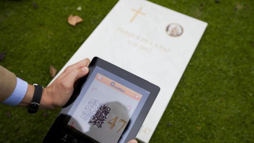Un hombre lee con su tableta el código QR impreso en una de las lápidas del cementerio Parque de la Paz de Chiva.