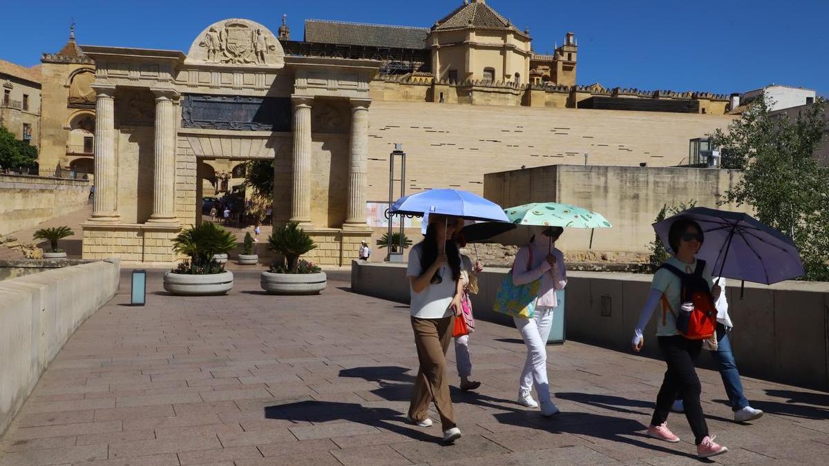 Varios turistas se protegen del calor con sombrillas mientras pasan por el puente romano.