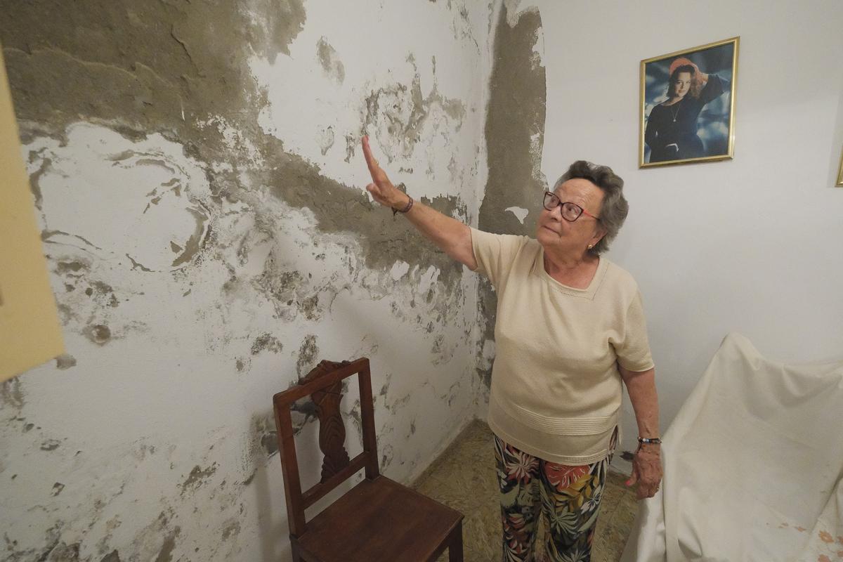 Celia Modesta enseña la pared de su salón afectada por las humedades.