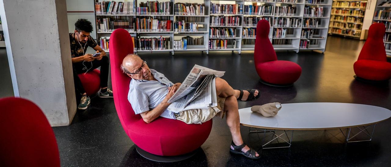 Un hombre echando una siesta y leyendo la prensa en una biblioteca de Barcelona, en plena ola de calor este julio