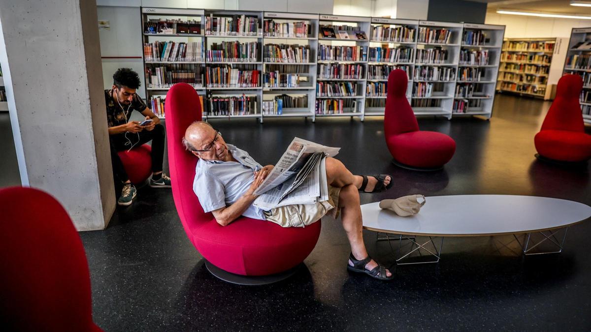 Un hombre echando una siesta y leyendo la prensa en una biblioteca de Barcelona, en plena ola de calor este julio