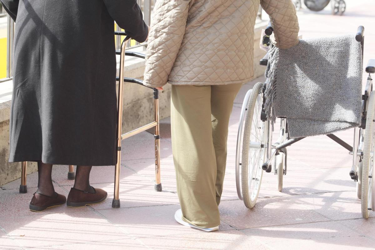 Una mujer sostiene un andador y, a su lado, otra una silla de ruedas en una calle de Murcia.