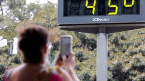 Una mujer toma una fotografía de un termómetro urbano marcando 45º.