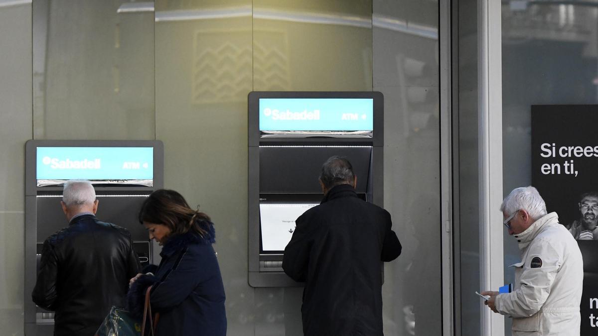 Varias personas haciendo uso de los cajeros de un banco de Murcia, este martes por la mañana.