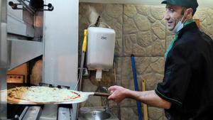Un cocinero coloca una pizza en el horno en la Pizzeria Origano de Figueres.