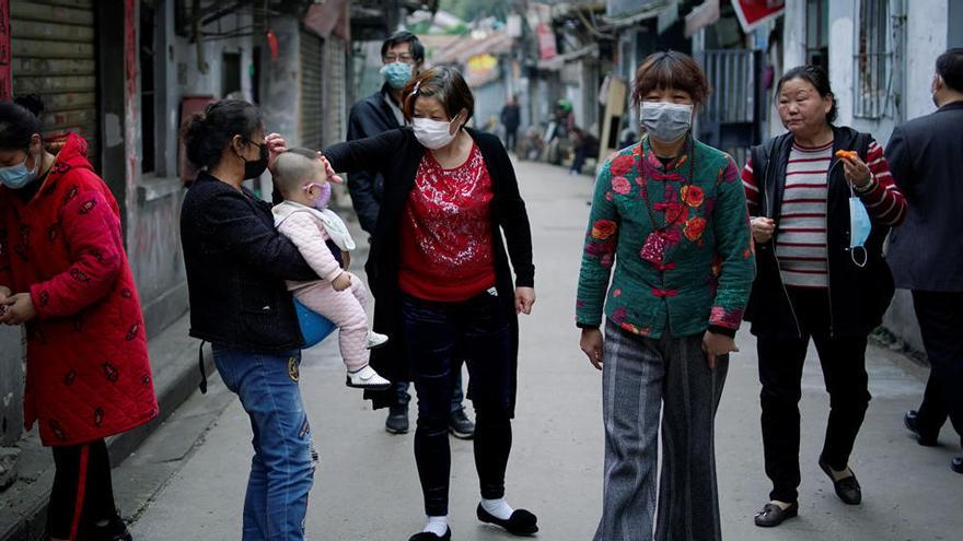 Residentes con máscaras faciales caminan en una vieja comunidad residencial bloqueada por barreras en Wuhan.