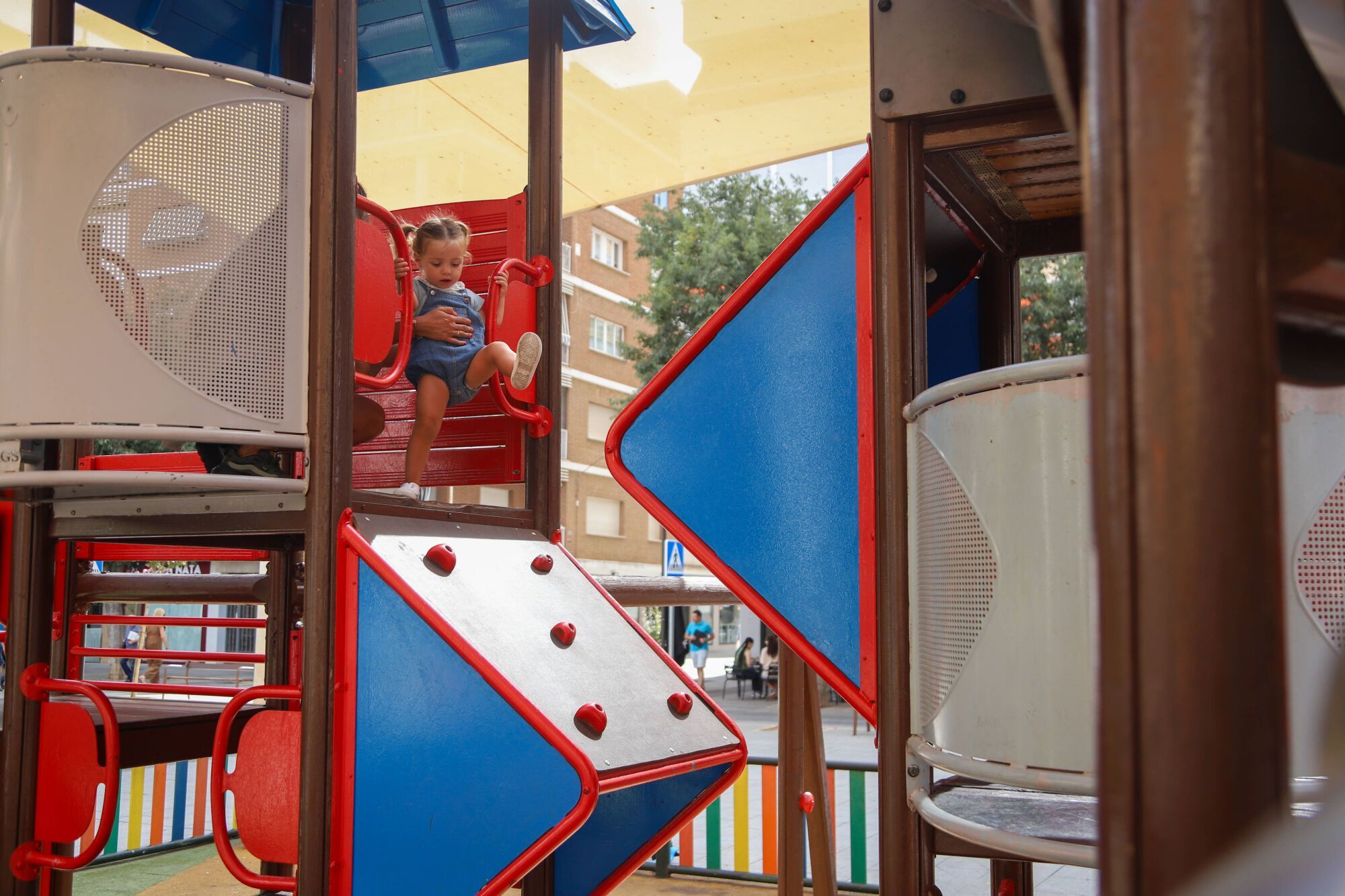 Una niña de 2 años, junto al módulo de juegos que preocupa a las familias por el riesgo de accidentes.