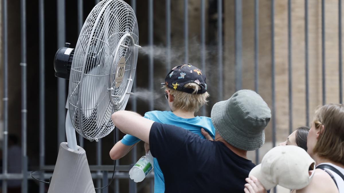 Turistas se refrescan en un ventilador en la calle.