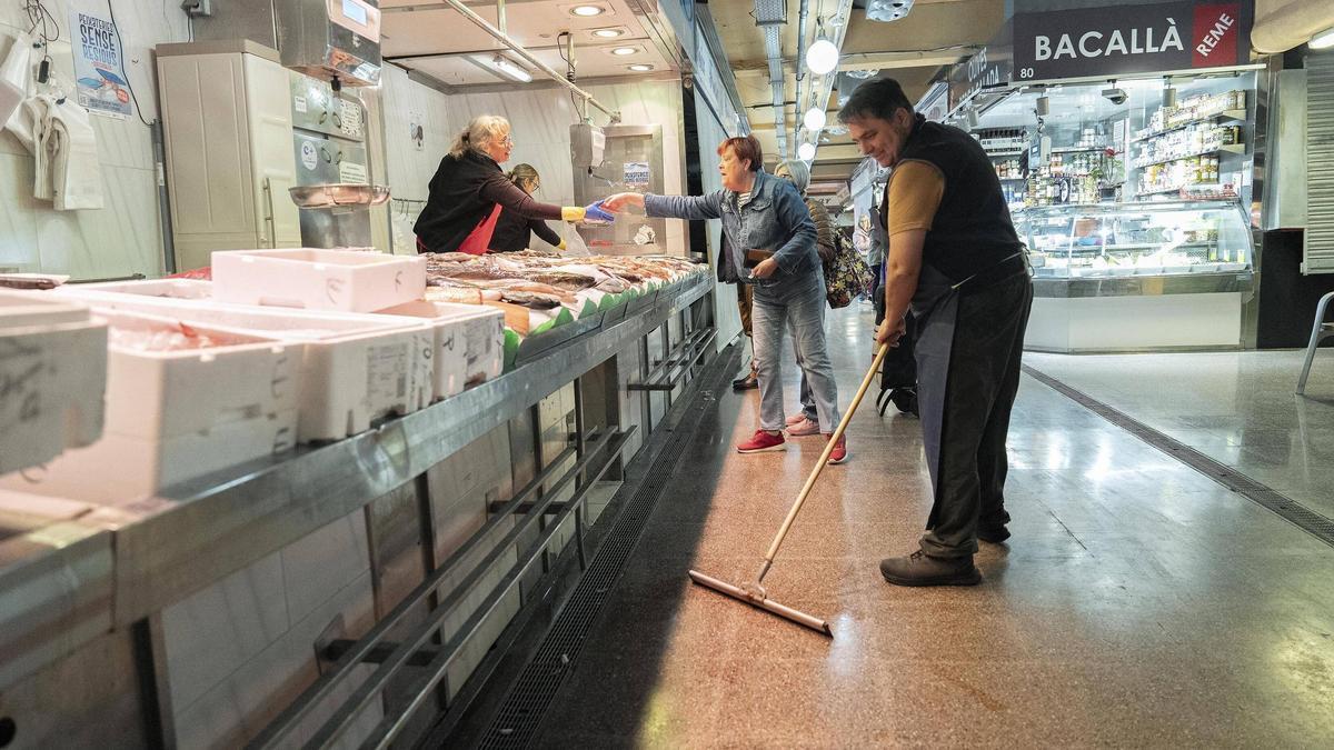 Un comerciante retira el agua de las baldosas junto a una pescadería del mercado de Sant Martí, en Barcelona.