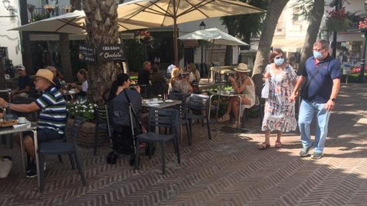 Varias personas con mascarilla junto a una terraza.