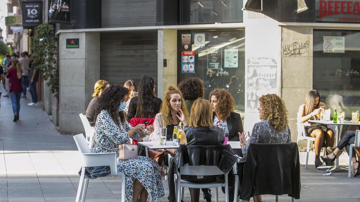 Jóvenes en una terraza frente a un local de ocio cerrado.