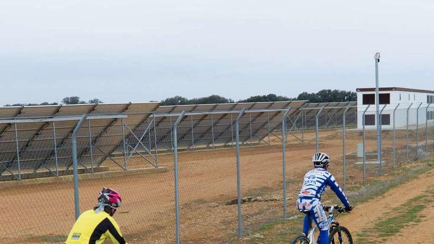 Dos ciclistas pasan frente a una instalación de placas solares.