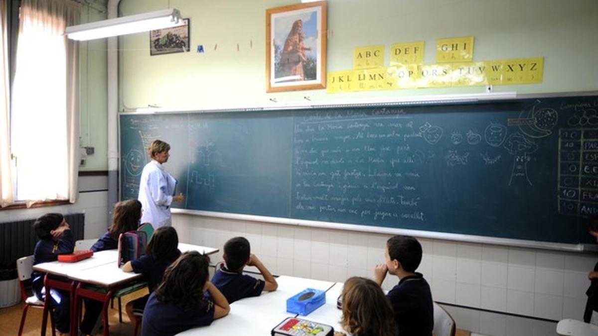 Una profesora da clases a niños de segundo de Primaria en un colegio de Lleida con una imagen de una Virgen en la pared frontal.