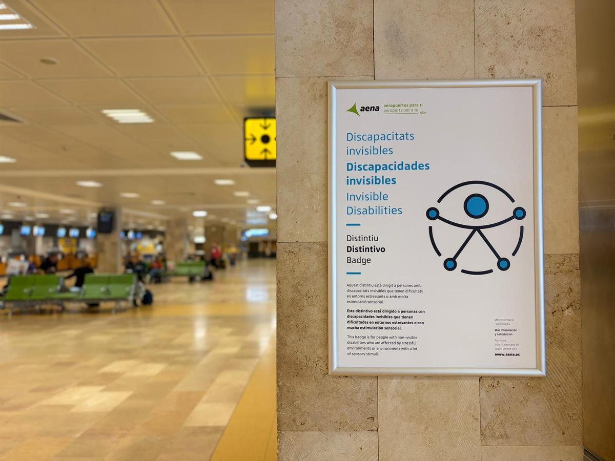 Un cartell d’Aena informa sobre el distintiu per a passatgers amb discapacitats invisibles a l’interior de l’Aeroport de Girona-Costa Brava