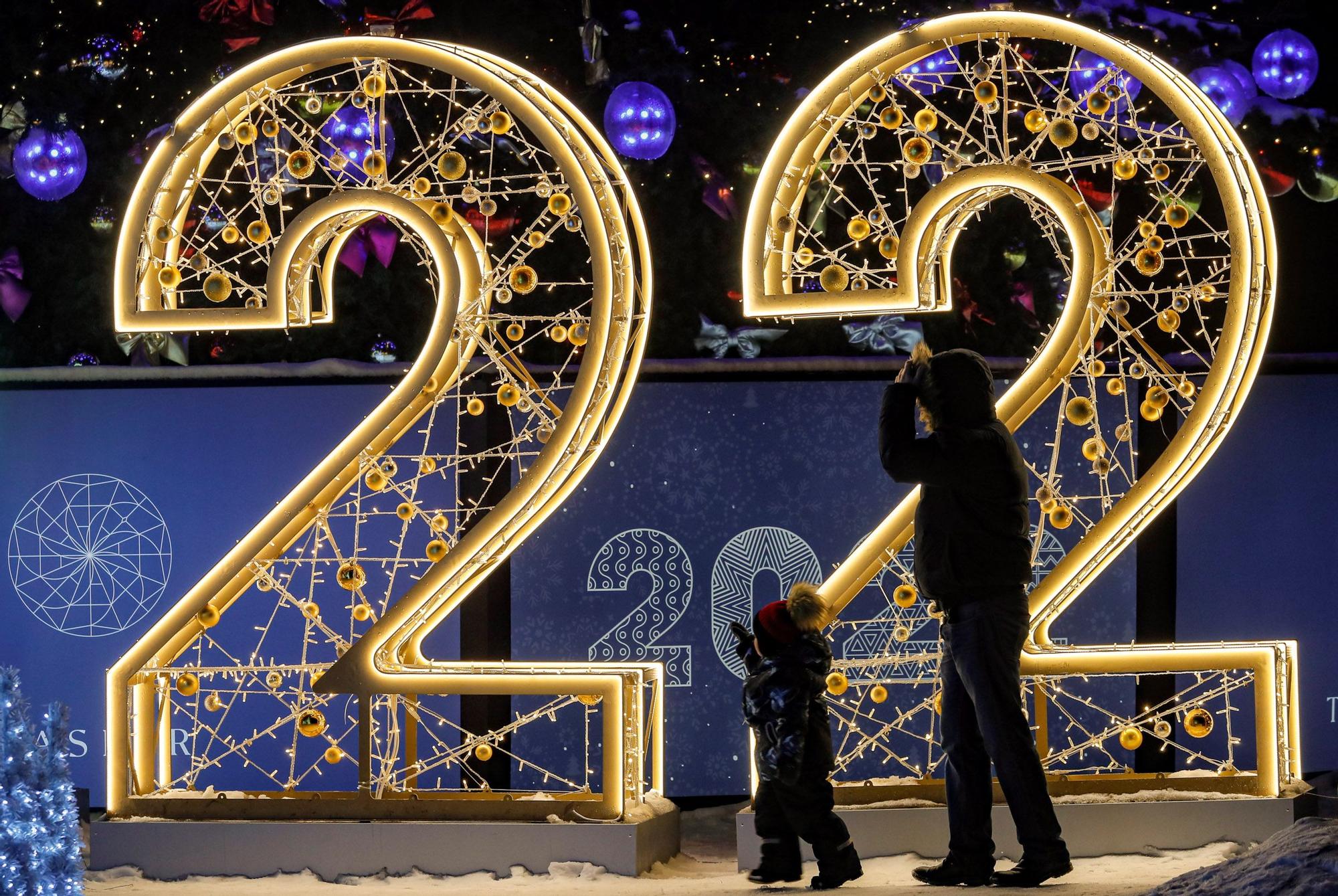 Moscú (Federación de Rusia), 16/12/2021.- Un hombre con su hijo camina frente a una escultura de luz '2022' instalada como parte de una decoración de temporada para las vacaciones de Año Nuevo y Navidad en Moscú, Rusia, 16 de diciembre de 2021 La celebración del Año Nuevo en el centro de Moscú puede verse parcialmente limitada debido a la pandemia en curso de la enfermedad COVID-19 causada por el coronavirus SARS-CoV-2. Se han instalado más de cuatro mil estructuras ligeras en el centro de la capital y sus barrios periféricos. (Rusia, Estados Unidos, Moscú)