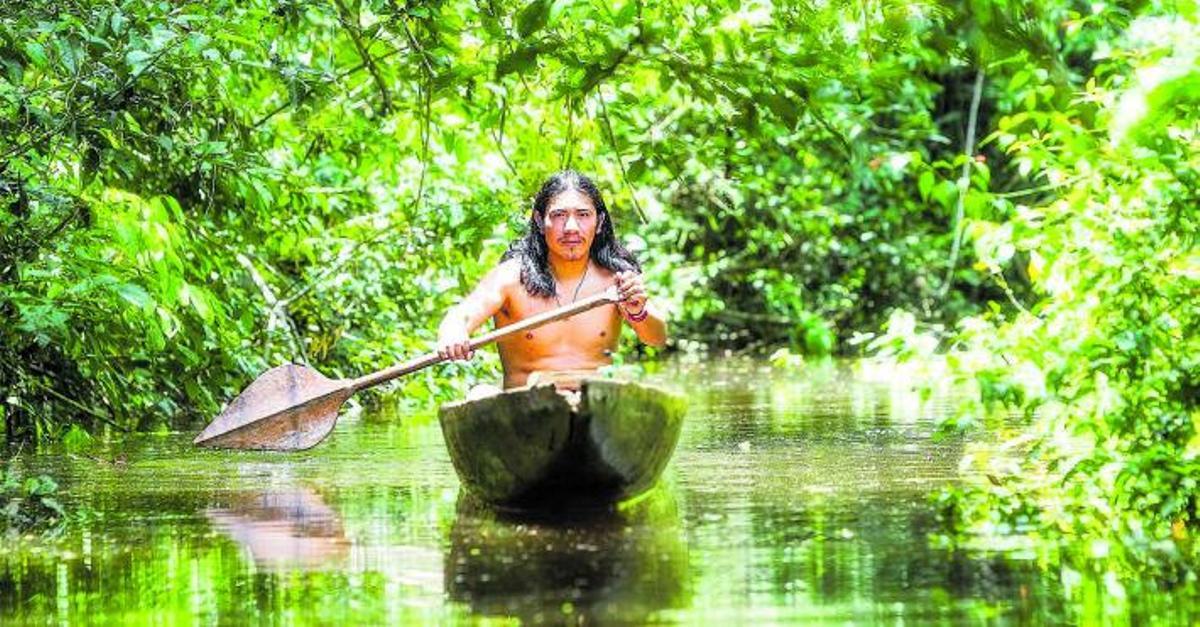Un indígena de la Amazoníanavega con su canoapor un río.  shutterstock