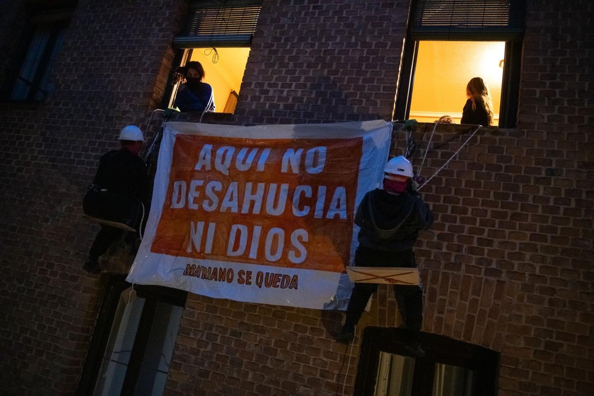 Varias personas cuelgan una pancarta de la fachada de la calle Carnero.