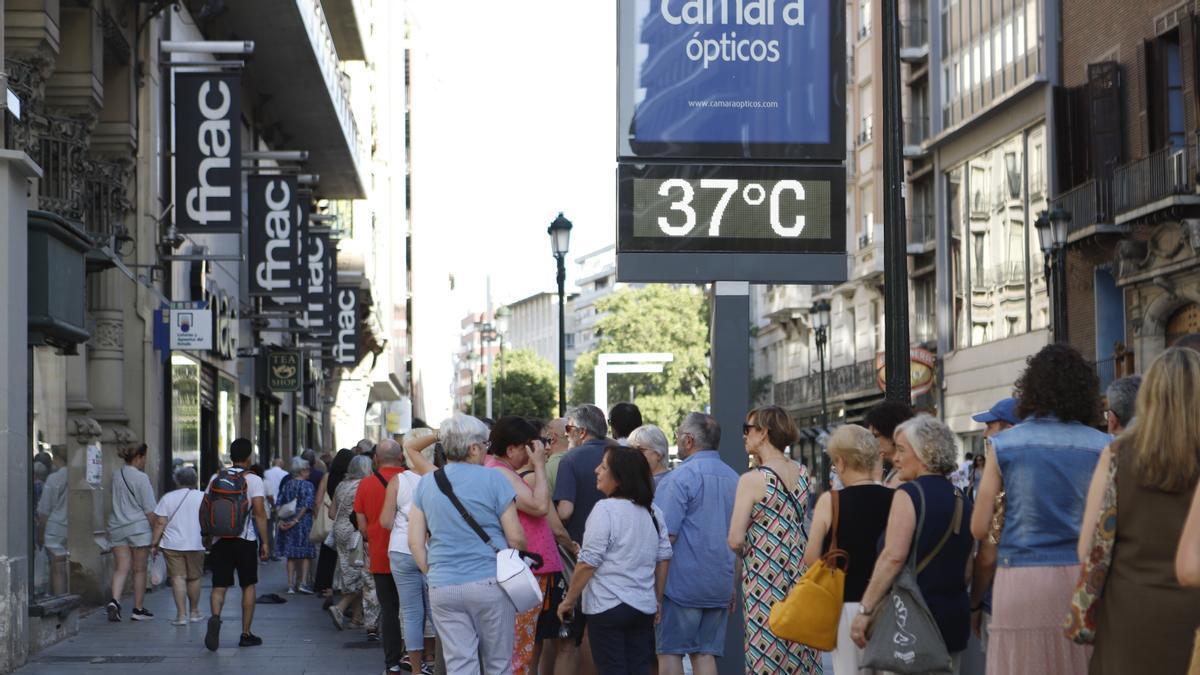 Varias personas hacen fila mientras un termómetro marca 37 grados en el Coso