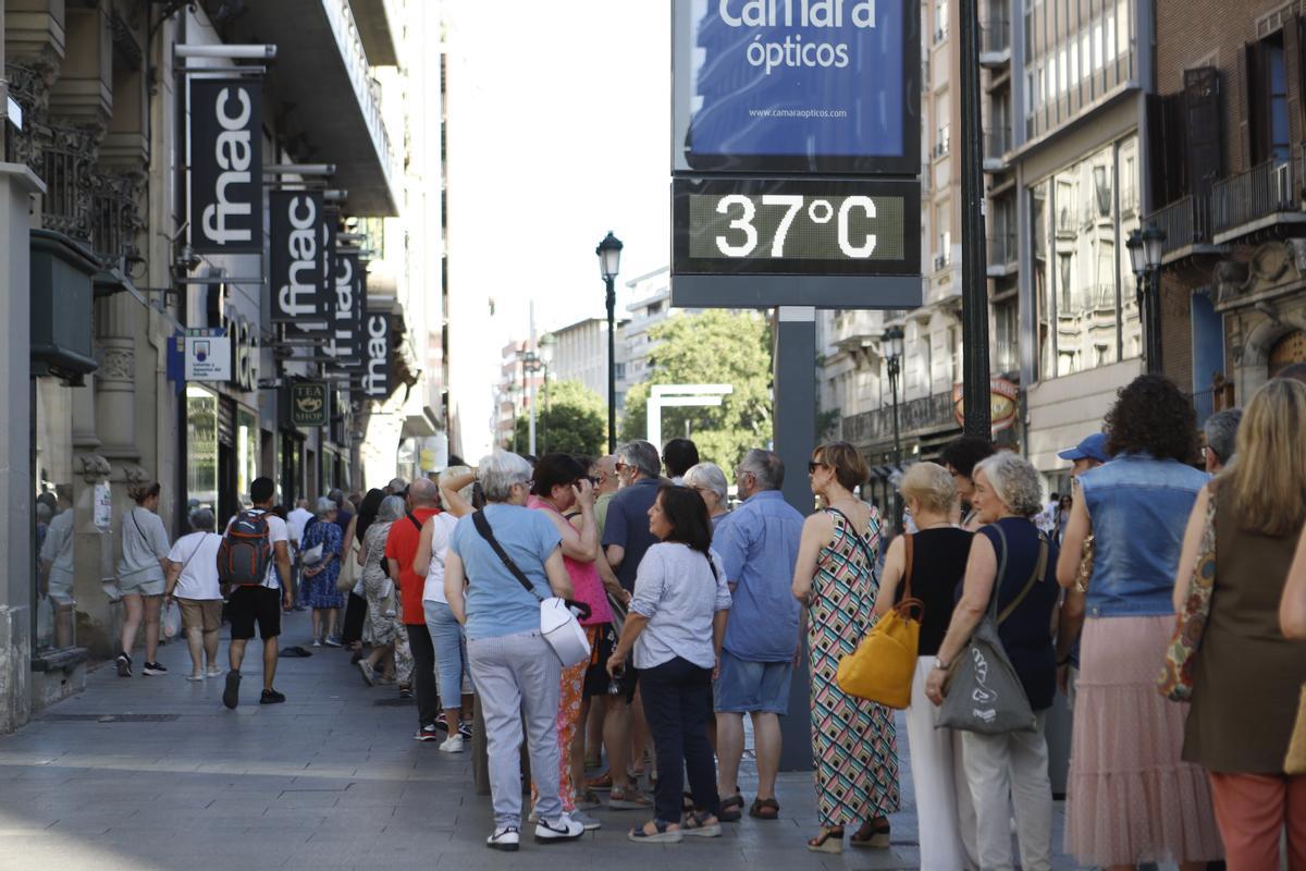 Varias personas hacen fila mientras un termómetro marca 37 grados en el Coso
