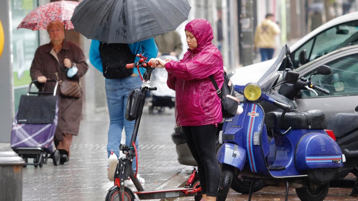 Viandantes con paraguas y una joven protegida con un chubasquero, en una mañana lluviosa en Córdoba.