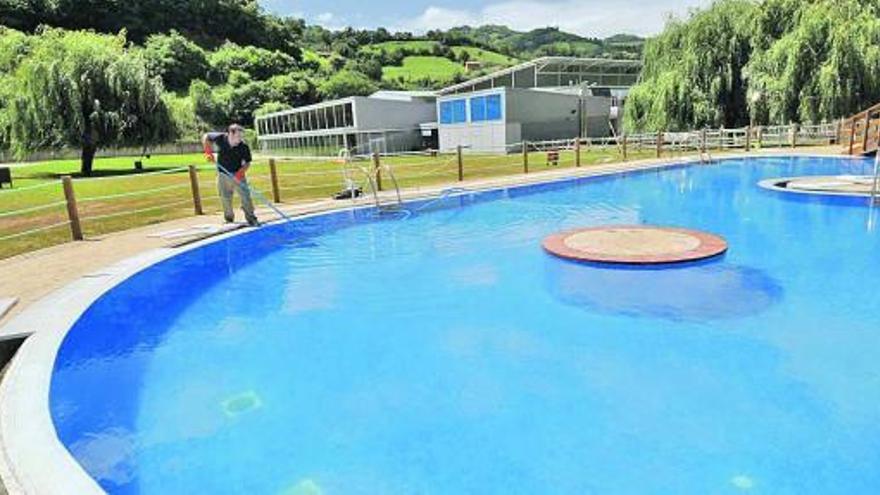 Un operario, realizando labores de mantenimiento en la piscina exterior de Pola de Lena, con la cubierta al fondo.